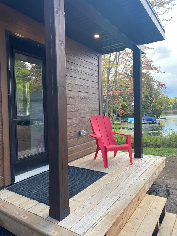 A wooden deck with a red chair, a window, and a view of a lake with boats.