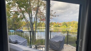 Une terrasse dotée de deux chaises abritées, offrant une vue sur un lac, et agrémentée d’une rambarde en métal.