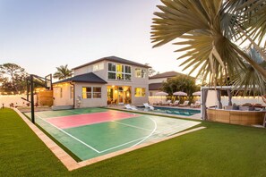 Ein zweistöckiges Haus mit Basketballplatz, Pool und überdachter Sitzgelegenheit.