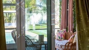 Ein Zimmer mit Blick auf einen Pool, einem Tisch mit Stühlen und einem Bett mit floralen Kissen.