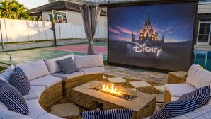 Ein gemütlicher Außenbereich mit Feuerstelle und einem großen Bildschirm mit Disney-Motiven.