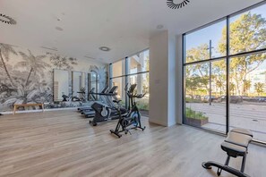 Ein geräumiges Fitnessstudio mit Trainingsgeräten, großen Fenstern und Wandmalerei.