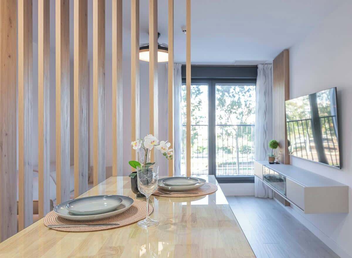 Un comedor con una mesa de madera, platos, una copa y un jarrón con flores.