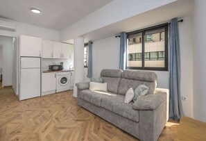 A compact living space with a kitchenette, a grey sofa, and a window with curtains. - Central Marbella Apartment with City Views (Marbella)