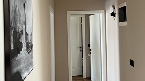 A hallway with a door at the end, a wall-mounted picture, and a light switch.
