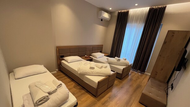 A hotel room with a bed, a sofa bed, a wooden cabinet, and a window with curtains.