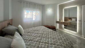 Ein Schlafzimmer mit Bett, Nachttisch, Spiegel und einem Fenster mit Vorhängen.