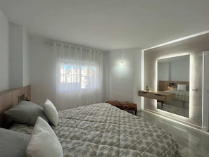 Une chambre à coucher avec un lit, une table de chevet, un miroir et une fenêtre avec des rideaux.