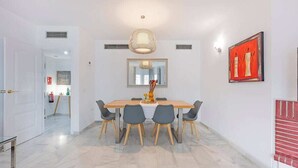 Ein Essbereich mit Holztisch und -stühlen, einer Hängelampe, einem Spiegel und einem gerahmten Kunstwerk an der Wand.