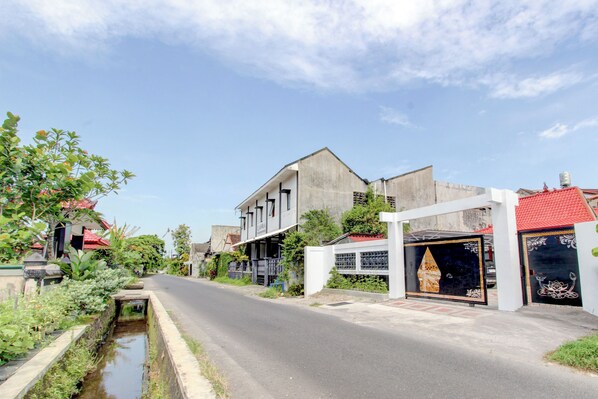 A residential street with houses, a narrow water channel, and a gated entrance with decorative elements. - Hotel O near Plaza Ambarukmo formerly (Banguntapan)