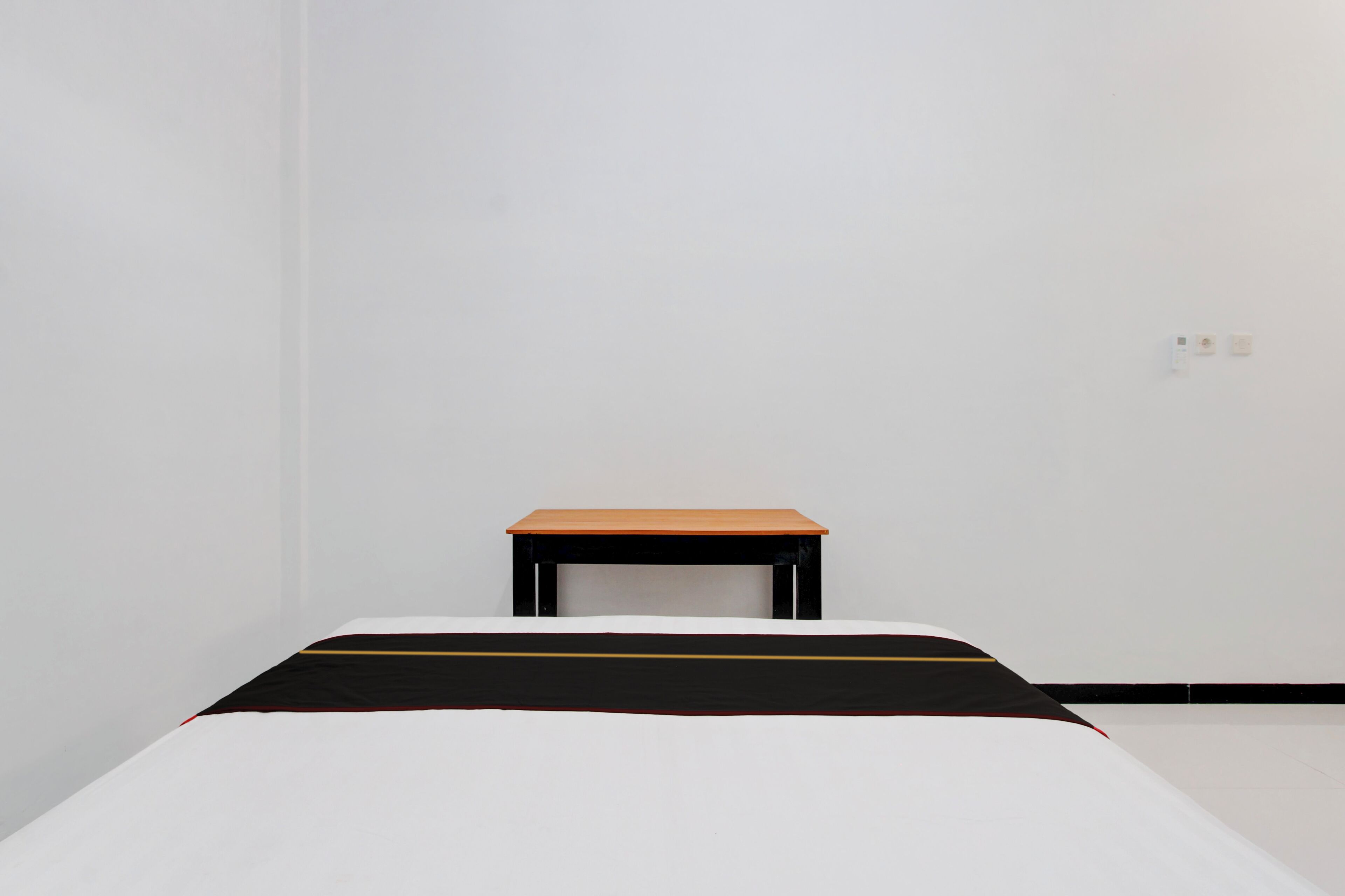 Una habitación minimalista con una cama, una mesita y una pared lisa.