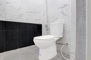 A white toilet with a black panel, a marble wall, and a tiled floor. - Hotel O near Plaza Ambarukmo formerly (Banguntapan)