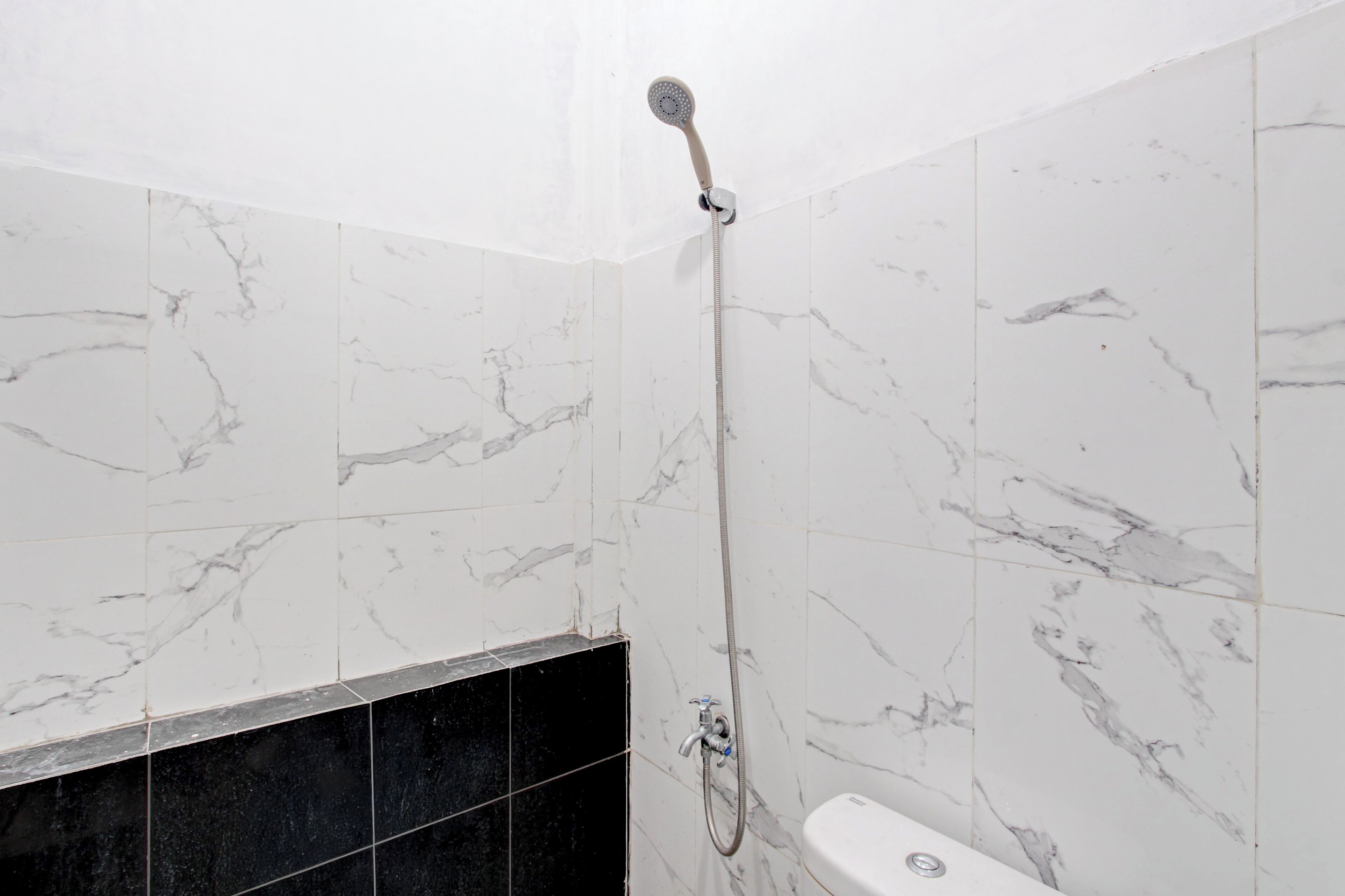 A bathroom with white marble walls, a black marble shower area, and a white toilet.
