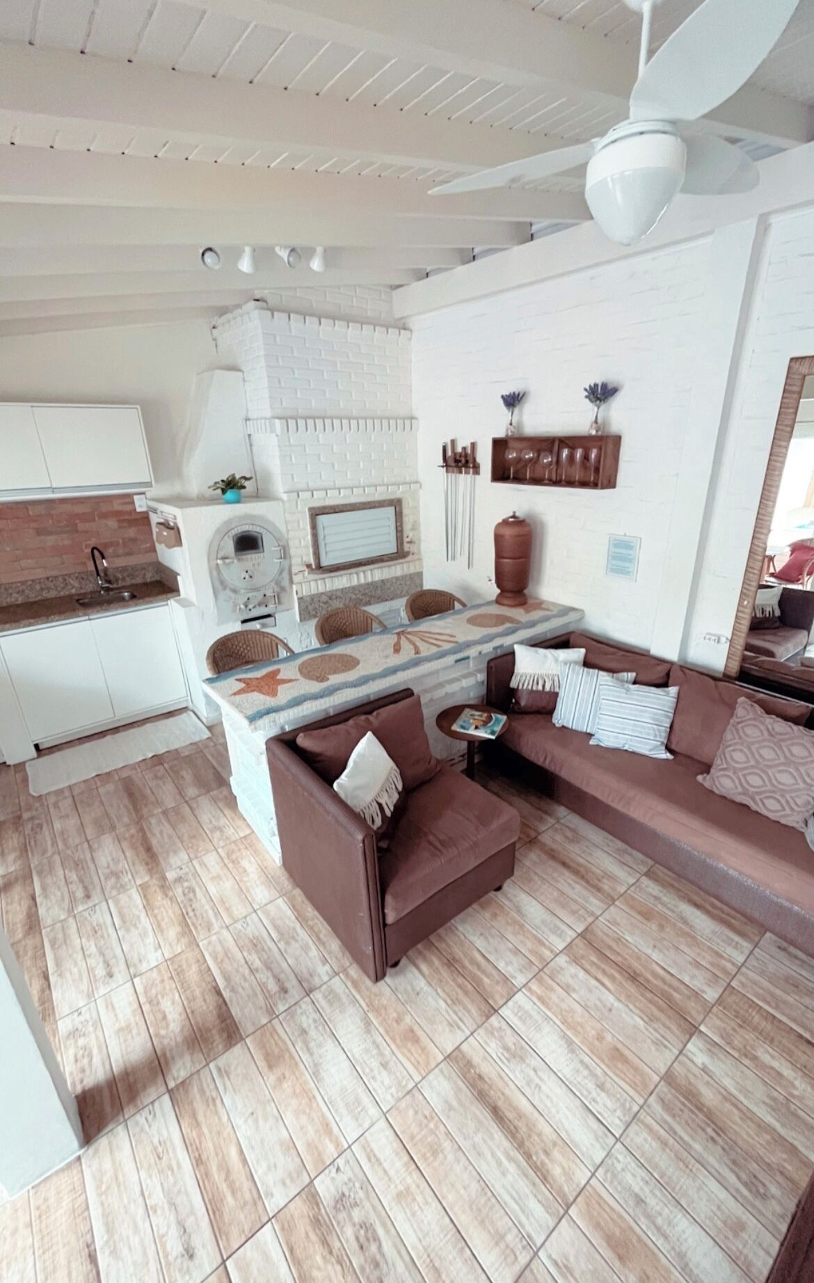 A modern kitchen with white appliances, a dining area with a brown sofa and a small table, and a ceiling fan.
