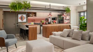 A modern living room with a sofa, ottoman, and a dining area with chairs and a table. - Flat de 100m2 com Serviço de Camareira (Sao Paulo)