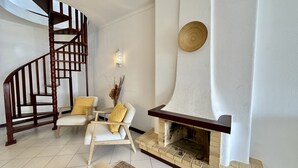 Uma escadaria, dois poltronas com almofadas, uma lareira e um aplique de parede.