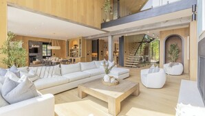A spacious living area with a large sofa, a wooden coffee table, and white chairs. There is a staircase leading to an upper level. - Lake Joseph Beach house - Bringing the Caribbean to Muskoka (MacTier)