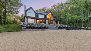 A modern house with a stone facade, large windows, and a stone staircase leading to the entrance. - Lake Joseph Beach house - Bringing the Caribbean to Muskoka (MacTier)