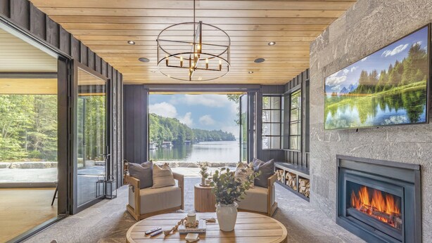 A modern living room with a fireplace, large windows, and a view of a lake. - Lake Joseph Beach house - Bringing the Caribbean to Muskoka (MacTier)