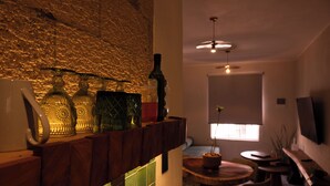 A room with a stone wall, a wooden shelf with glass bottles, a round table, and a TV mounted on the wall. - 15min from downtown,20min airport,5min walking cenote corazon & ZAMNA Festival. (Aldea Tulum)