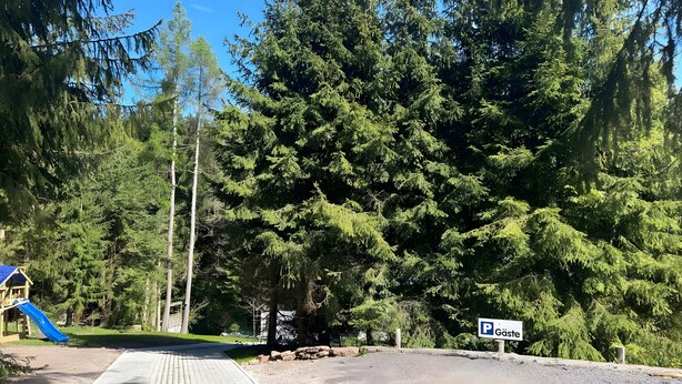 A parking area with a sign indicating 'Gäste' (guests), surrounded by dense forest and a playground with a blue slide. - Vacation with Dog – Holiday Home for up to 5 Guests (Friedrichroda)
