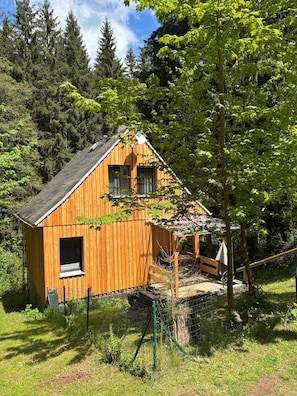 Eine Holzhütte mit geneigtem Dach, einem Fenster und einer kleinen Veranda.