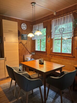 Interior de madeira com uma mesa de jantar, cadeiras, um relógio e uma janela com cortinas.