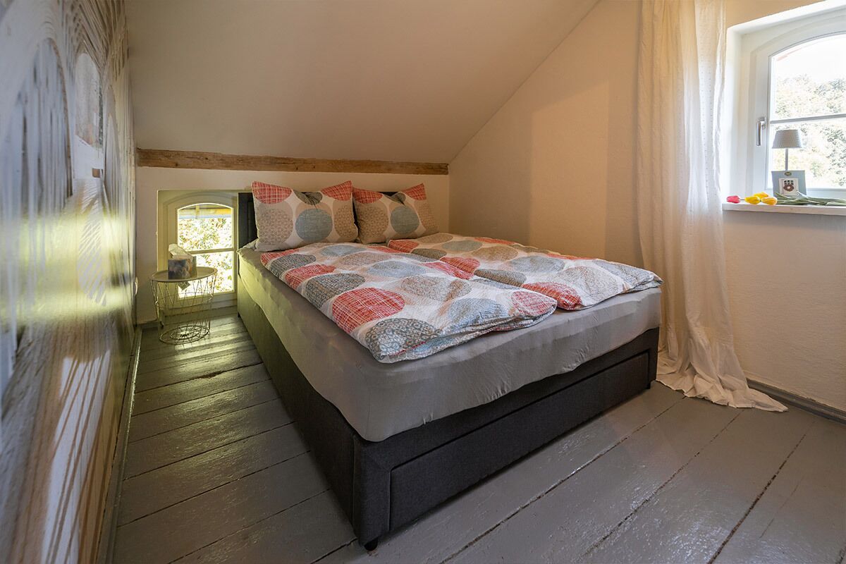 A bedroom with a bed, a window with curtains, a bedside table, and a lamp.