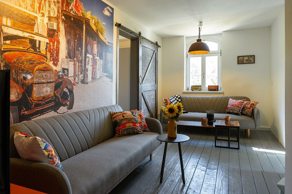 A living room with a sofa, a small table with a vase, a bench, and a mural on the wall.