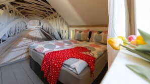 A bedroom with a wooden ceiling, a bed with patterned bedding, and a window with flowers. - Nice American Diner Holiday apartment (Penig)
