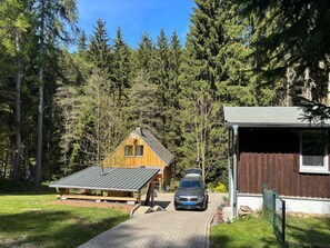 Eine Hütte mit parkendem Auto davor, umgeben von einem Wald.