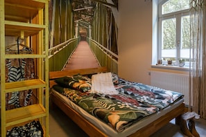 Un dormitorio con una cama de madera, una ventana con cortinas y vistas a un puente, y una estantería con ropa.