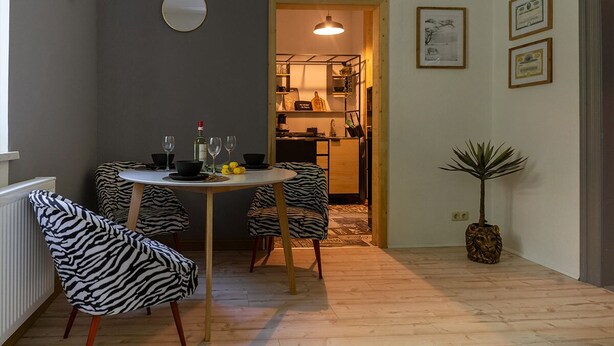 A dining area with zebra-patterned chairs, a round table, and a potted plant.