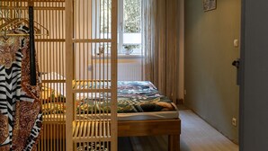 A room with a bed, a wooden partition, a window with curtains, and a view of trees outside.