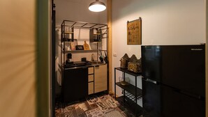 A compact kitchen with a black refrigerator, a hanging pendant light, and a wall-mounted sign.
