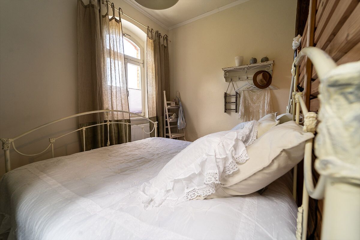 A bedroom with a bed, curtains, a radiator, and a shelf with items.