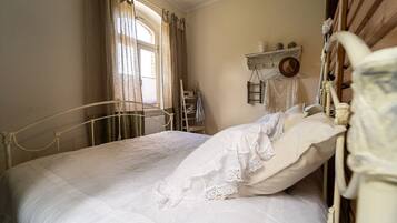 A bedroom with a bed, curtains, a radiator, and a shelf with items.