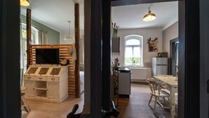 Une pièce comprenant un meuble TV en bois, un buffet blanc, une table à manger avec des chaises, un coin cuisine avec un réfrigérateur et une fenêtre donnant sur un beau paysage.