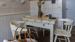 Une cuisine rustique avec une table en bois, des chaises blanches, un panier en osier et un vase rempli de fleurs.