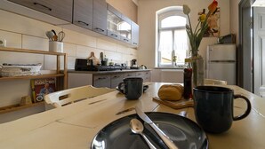 Une cuisine avec une table à manger dressée pour deux personnes, un réfrigérateur et une fenêtre ornée de fleurs.
