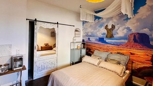 A bedroom with a bed, a nightstand, a coffee machine, a mural of a desert landscape, and a hanging light fixture. - Little Honeymoon Suite (Penig)