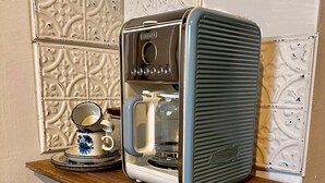 A vintage coffee maker on a wooden table with a decorative wall in the background. - Little Honeymoon Suite (Penig)
