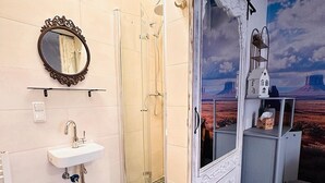 A bathroom with a shower, a sink, a mirror, and a decorative wall with a desert mural. - Little Honeymoon Suite (Penig)