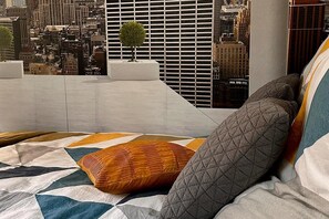 Un lit avec un oreiller matelassé et une vue sur le paysage urbain par la fenêtre.