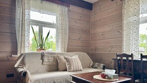 Una habitación acogedora con un revestimiento de madera, un sofá color beige, una mesa de centro de madera y una ventana con cortinas.