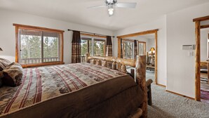 Une chambre à coucher avec un grand lit, une tête de lit en bois, un ventilateur de plafond et de grandes fenêtres avec des rideaux.