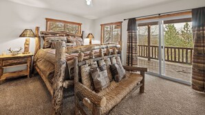 Une chambre à coucher avec un grand lit, un banc en bois, un ventilateur de plafond et une vue sur l’extérieur, accessible par une porte-fenêtre coulissante.