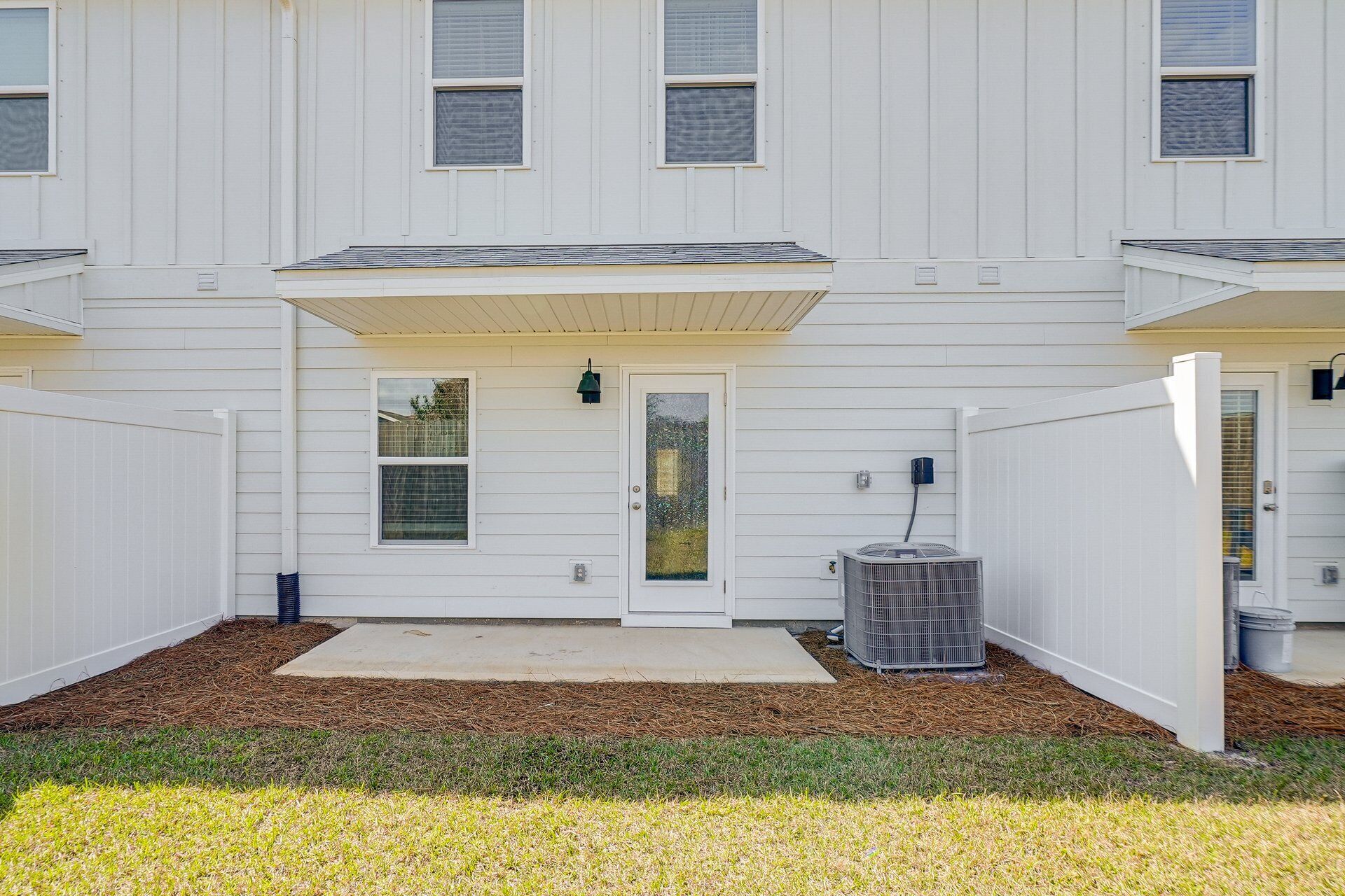 A two-story building with a front porch, a garage door, and a small front yard with grass and mulch.
