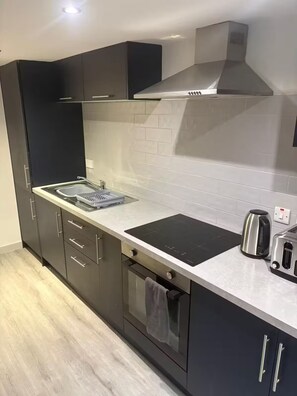 Eine moderne Küche mit dunklen Schränken, einer Edelstahl-Dunstabzugshaube, einem eingebauten Backofen und einer Arbeitsplatte mit Wasserkocher und Toaster.