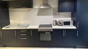 Een moderne keuken met donkere kastjes, een magnetron, waterkoker en een inbouwoven.